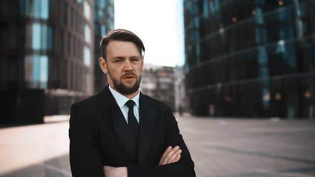 4K. UHD. Portrait of Young successful beard businessman in suit and tie disgusted with Your opinion. He looks mistrust with crossed hands. Head denial. Sunny morning teal and orange middle shot