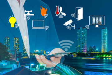 Smart Building and Internet of Things concept. Smart building management icons on Double Exposure image of Businessman use smart phone and City Building at night.