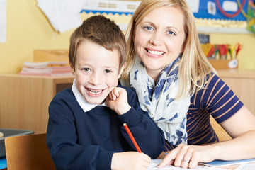 Teacher Helping Male Elementary Pupil Working At Desk