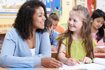 Teacher With Female Elementary School Pupil In Class