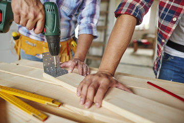 Man drilled a wooden plank and younger one helped