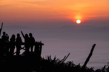 Fototapeta na wymiar Silhouette of tourists looking at sunrise vantage point atop a rainforest. Doi Ang Khang, Chiang Mai Province, Thailand.