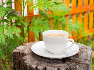 A cup of coffee on an old tree stump with small green garden background.