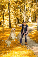 Fototapeta premium Young man walking a dog at the park in good weather. Boy and golden retriever. Autumn environment