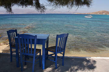 Mesa y tres sillas azules a los pies del mar en Naxos, islas griegas, Grecia