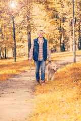 Fototapeta premium Young man walking a dog at the park in good weather. Boy and golden retriever. Autumn environment