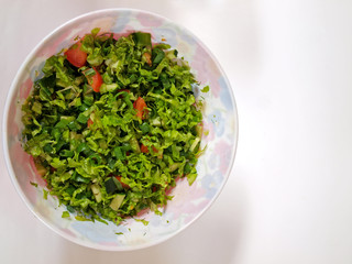 Plastic bowl with salad from lettuce and tomato close up on white background with copy space.