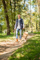 Naklejka na ściany i meble Young man walking a dog at the park in good weather. Boy and golden retriever. Autumn environment