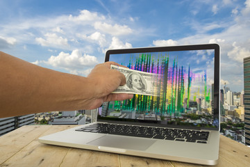 Fintech for investment concept image. Hand pull money out of computer screen with binary code againt City background. Representing fintech involved in investment business.