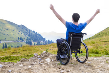 Optimistic handicapped man sitting on wheelchair on mountain.