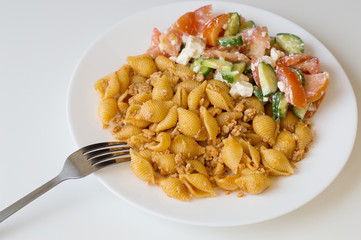 Italian pasta with chicken mince and salad with tomatoes, cucumber and feta cheese cubes on white plate with one fork
