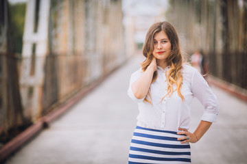 Fototapeta premium Very beautiful young girl is a teenager in a luxury Spanish women dress with her blond hair and a flower in her hair is romantic on the bridge over the river at sunset . Busines