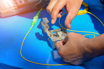 Technician using cleaver cutting optic fiber on blue table with