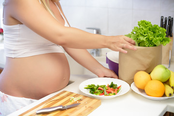 Obraz na płótnie Canvas pregnant woman at kitchen preparing salad, close up