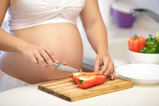 pregnant woman cuts the pepper in the kitchen, close up