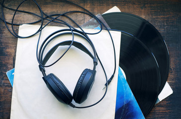 Vinyl, retro, earphones. Headphones and pile of old vinyl records on wooden  background