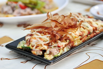 Close up Japan pizza as "Okonomiyaki" is fried mixed vegetable flour with meat topped sweet sauce ,mayonnaise or salad cream and sliced dried yellowfin tuna served with side dish. Selective focus.