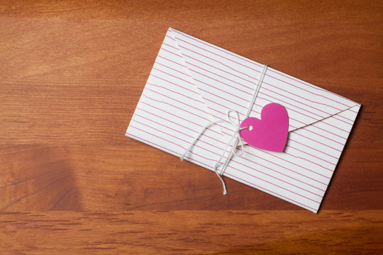 Envelope and red heart shape card tied with string on wooden table