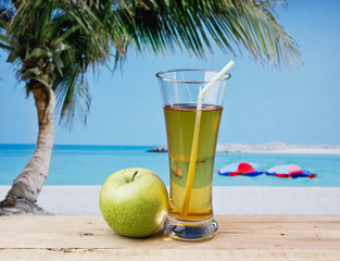 Glass of apple juice on a beach table