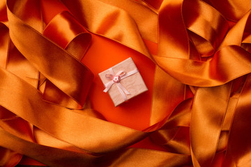 Top view of pink small gift box with ribbon on orange ribbon bac