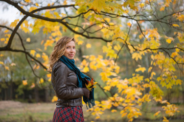 Beautiful girl blonde with wavy hair standing near the autumn tree with yellow leaves