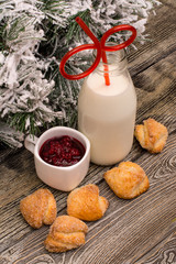 Fir branch in snow, bottle of milk with a straw, jam, cookies on wooden background