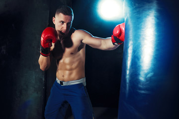 Male boxer boxing in punching bag with dramatic edgy lighting in a dark studio