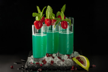 some glasses with green citrus drink and ice on a black stone on a dark background