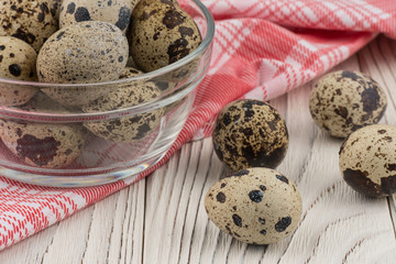 Quail eggs in a glass bowl on old white wooden table.