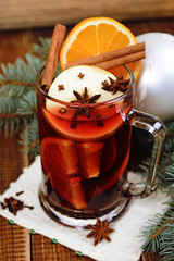  A glass of hot mulled wine with apple,orange and spices on a background of traditional Christmas decorations.