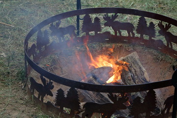 A campfire burning in a hand dug pit surrounded by a decorative metal fire ring.