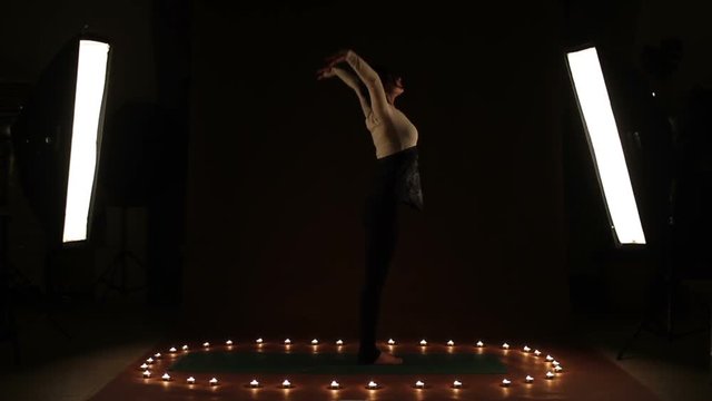A strong woman showing gymnastic exercise in the light of candles