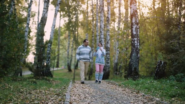 Young couple man and woman wear knitted sweater walking outdoor in autumn forest making selfie. 1920x1080
