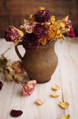 Dry roses in an old clay jug on a wooden surface. Vintage style still life with dried roses