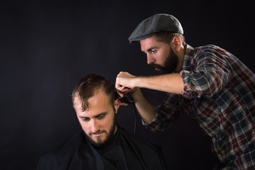 Barber shaves the hair to the client. On a black background.