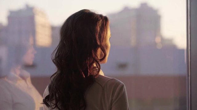 Young beautiful businesswoman admire cityscape at sunset in modern office with panoramic windows