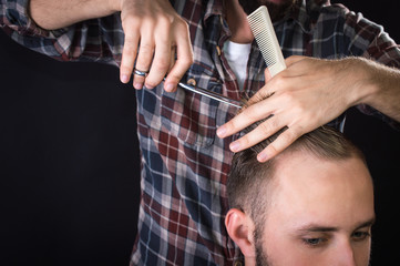 Obraz na płótnie Canvas Barber cuts client with scissors hair. On a black background.