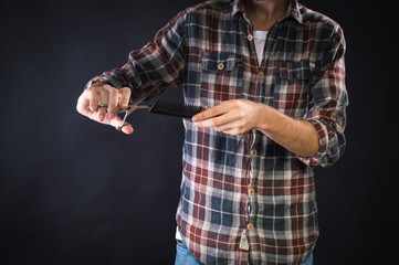 Barber holding scissors and comb. On a black background.