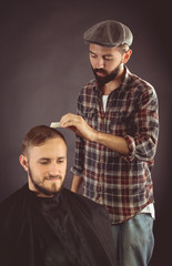 Barber combing the hair to the client. On a black background.