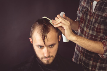 Barber combing the hair to the client. On a black background.
