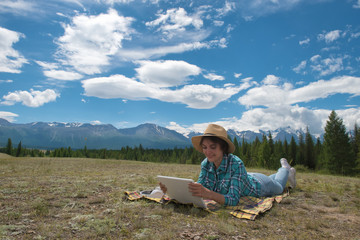 Beautiful young woman in the hat using tablet computer on mountains background outdoors.