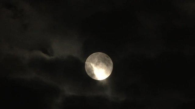 Clouds part and reveal bright full moon on cloudy night.