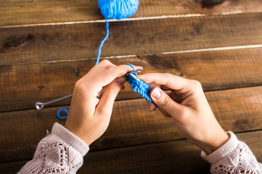 Women's hands are beginning to knit with blue thread. Rows related thread on the needles with a ball. On a wooden background.