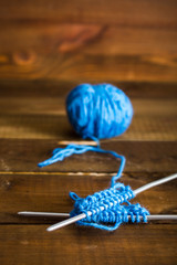 Start knitting with blue thread. Rows related thread on the needles with a ball. On a wooden background.