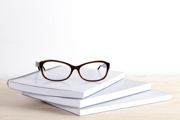 pile of exercise books and glasses on a white background and a wooden table. learning