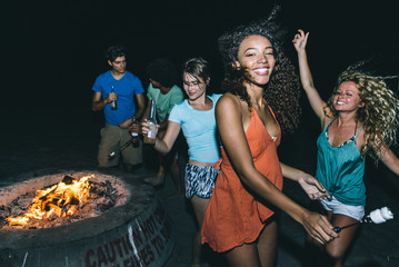 Group of friends making party on the beach with fire and music