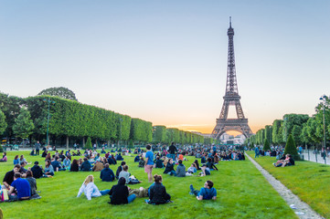 Naklejka premium Eiffel Tower and people sitting on the grass watching sunset in Paris, France