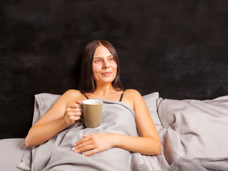 Woman lying in bed and drinking morning coffee. Beautiful young brunette going to have a breakfast...