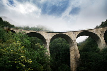 Fototapeta na wymiar Old stone bridge near green forest mountains