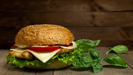 Home made hamburger with cheese, tomatoes and basil  on wooden background. Fastfood meal.